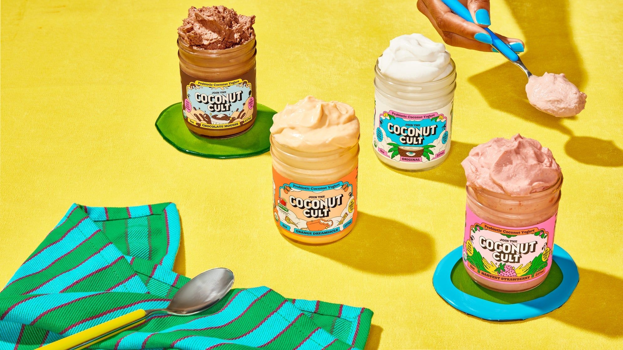 Jars of The Coconut Cult yogurt on a bright yellow table.